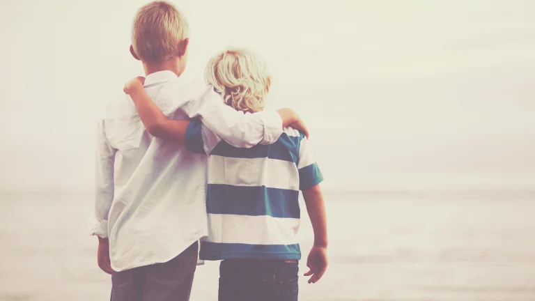 Two children standing together by the sea, representing support and connection
